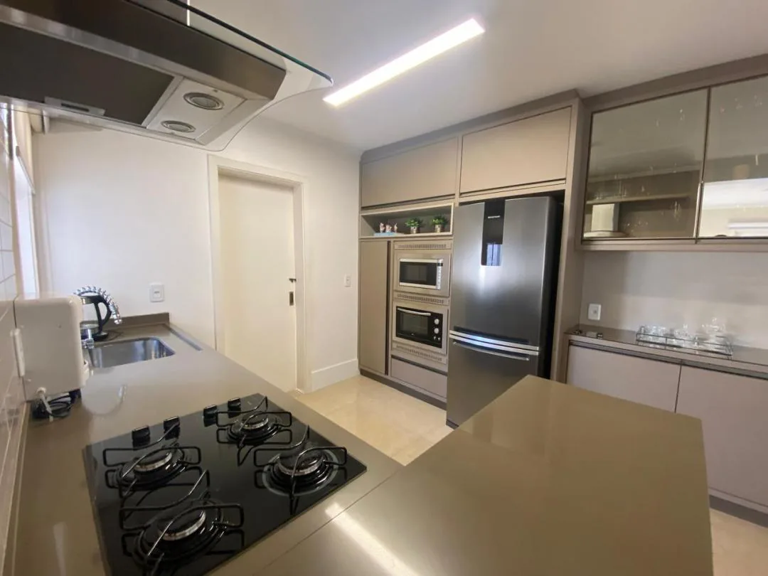 Cozinha planejada em tom bege com cooktop a gás, forno e micro-ondas embutidos e geladeira inox