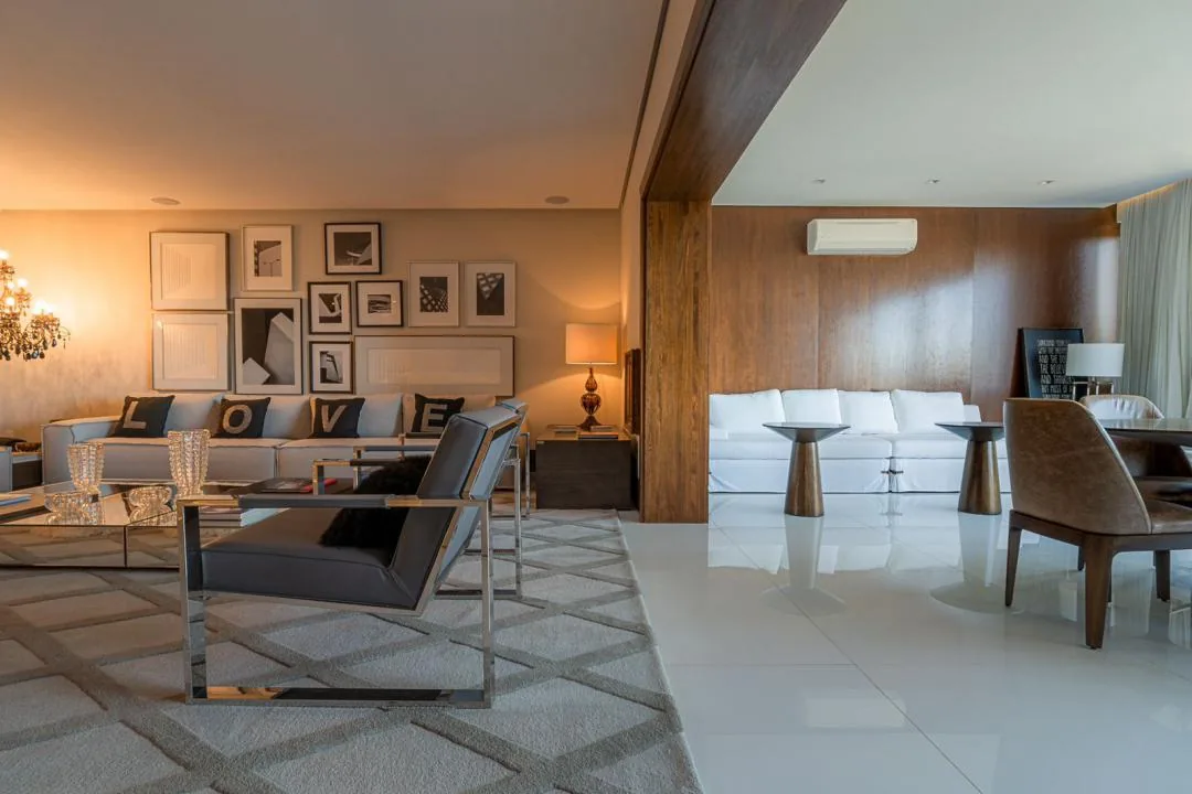 Sala de estar integrada a um ambiente com parede revestida de madeira, sofá branco e duas mesas laterais de pé metálico