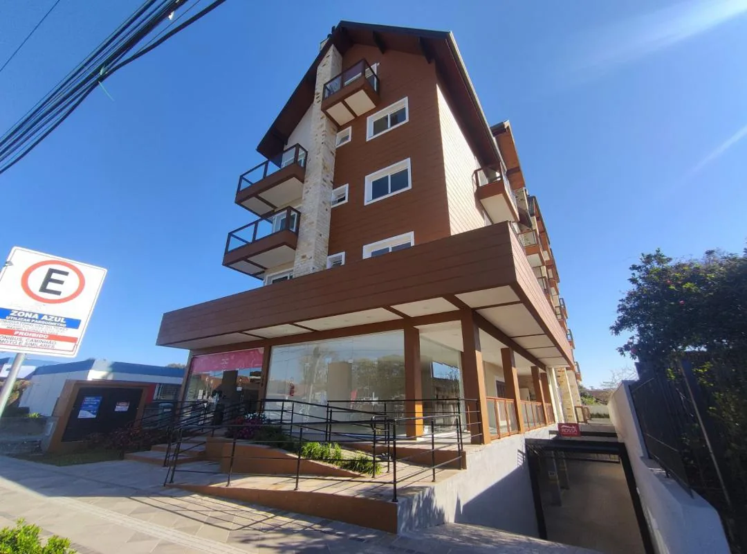 Fachada do prédio com revestimento amadeirado, coluna de pedra, sacadas com guarda-corpo de vidro, telhado inclinado e lojas envidraçadas no térreo