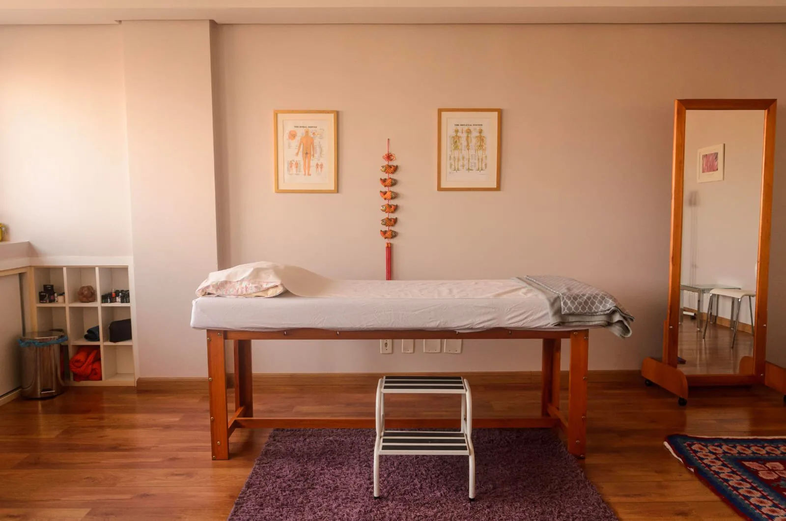 Parede da sala com dois quadros, maca de madeira sobre tapete roxo e espelho de chão