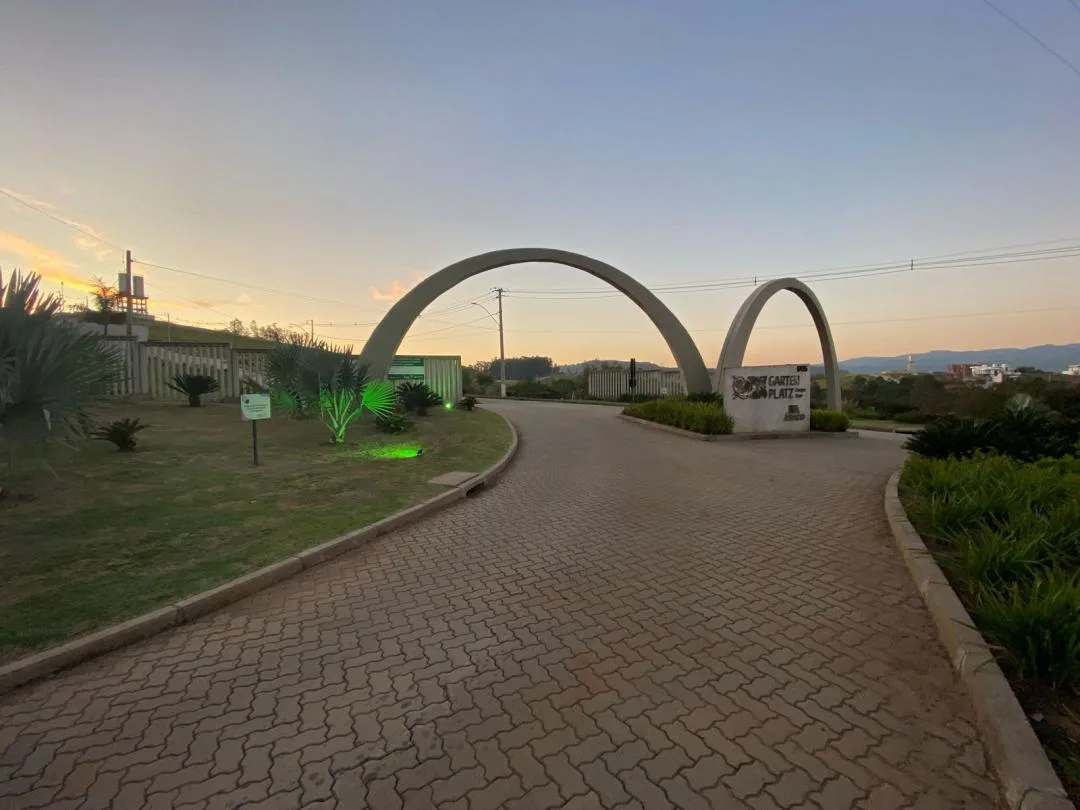 Portal de entrada do loteamento com dois arcos de concreto, monumento com o nome Garten Platz e rua de paver ao entardecer