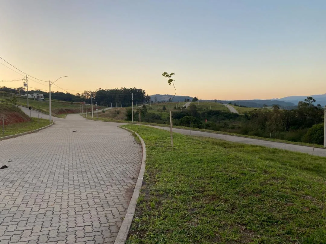 Rua de paver em curva entre gramados, com postes de luz e morros ao fundo