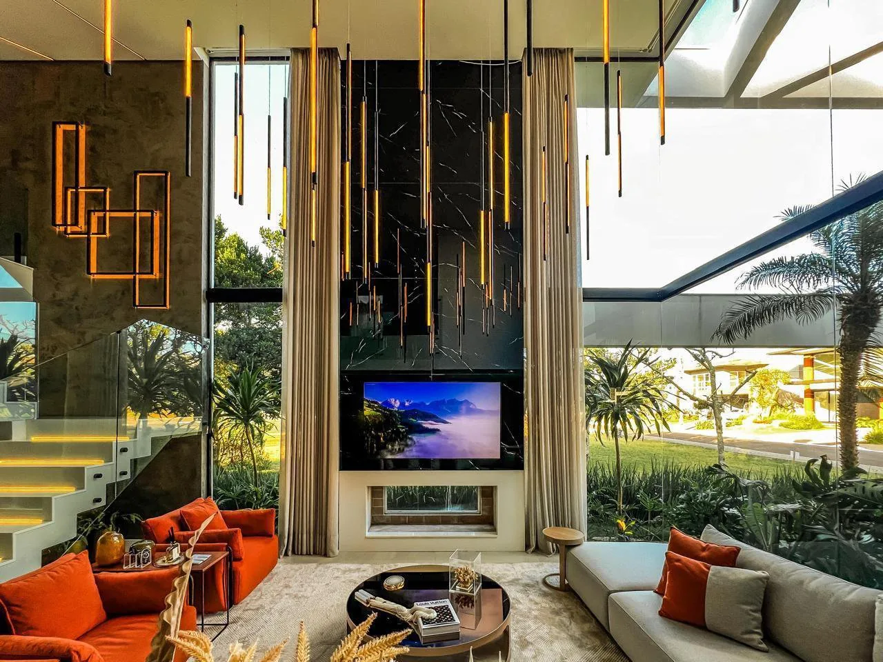 Sala com painel de mármore preto e TV, cortinas altas e janelas de piso a teto voltadas para o jardim