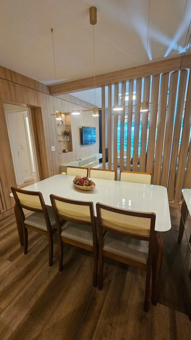 Mesa de jantar branca com seis cadeiras de madeira, pendentes e divisória ripada separando a sala