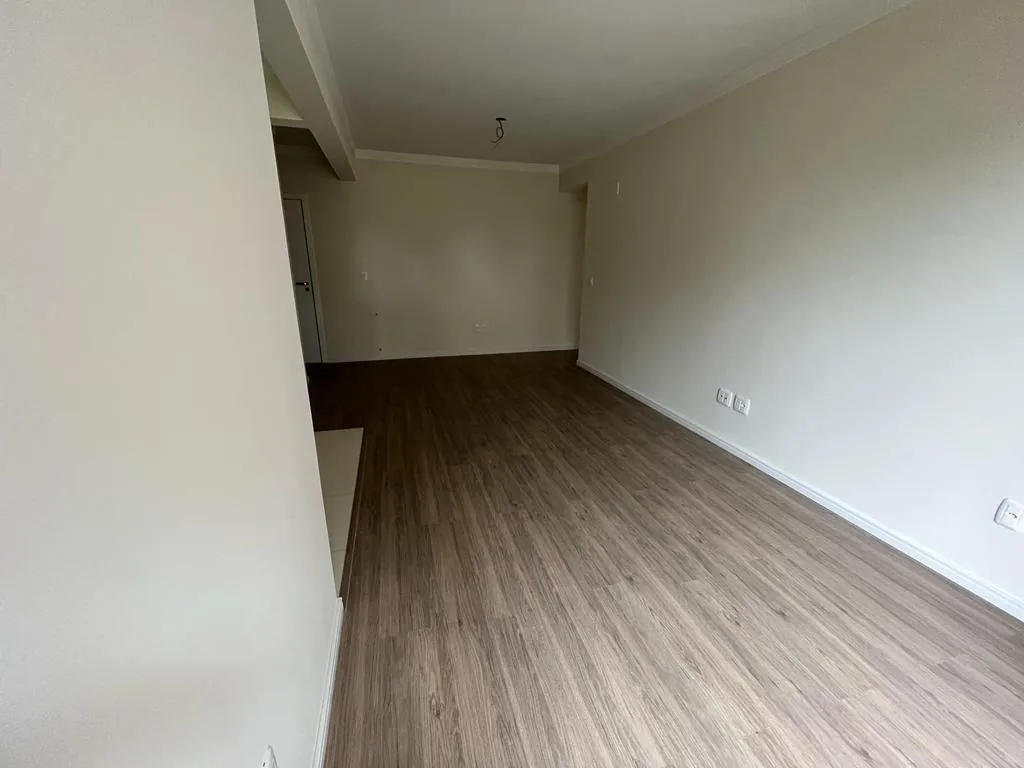 Sala em outro ângulo, com piso laminado, paredes claras e porta ao fundo