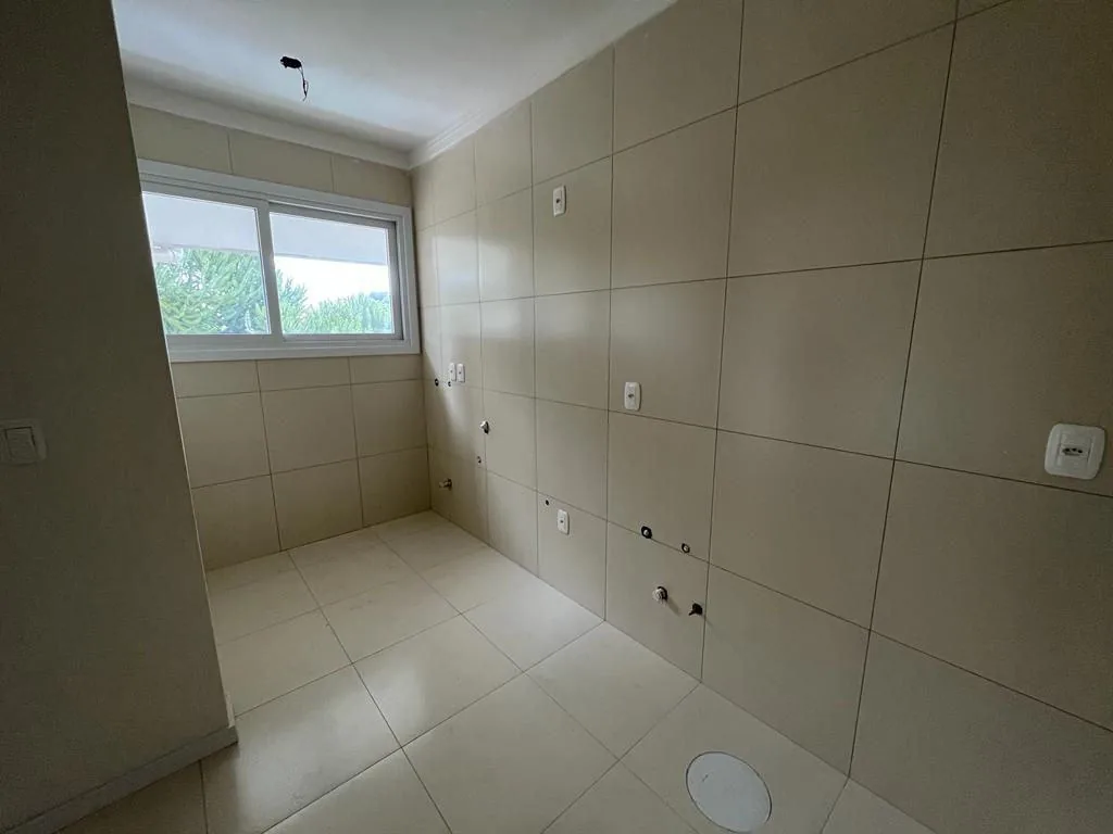Cozinha ainda sem armários, com paredes e piso em porcelanato claro, pontos hidráulicos e janela