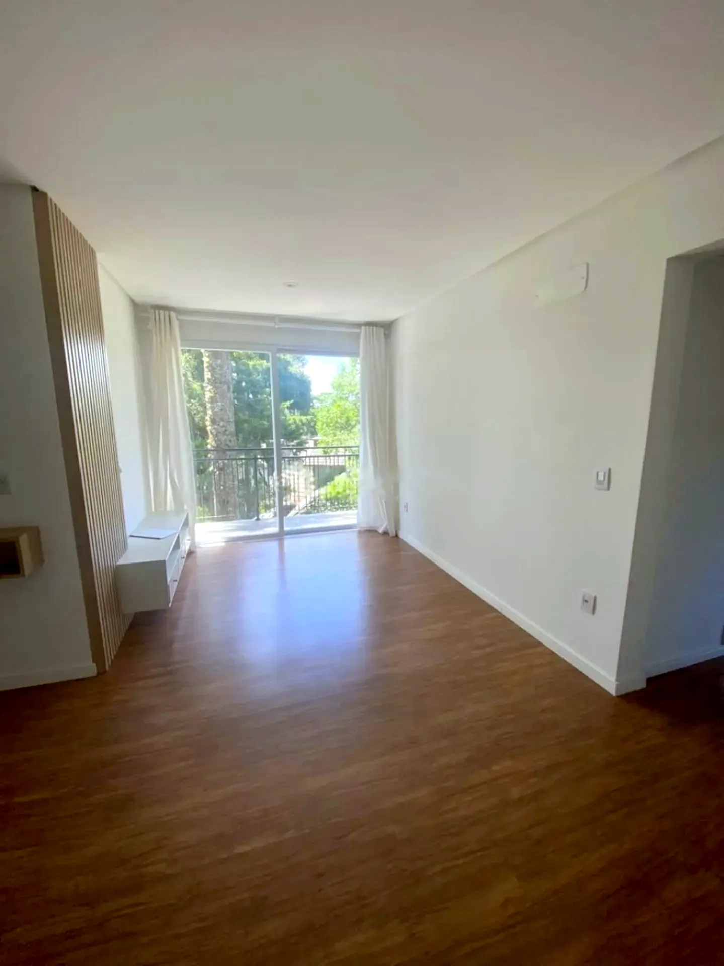 Sala com piso laminado e porta para a sacada, no Centro de Canela