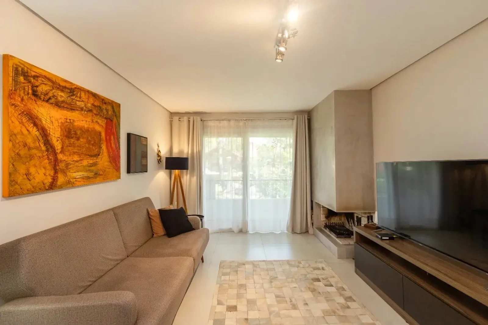Sala de estar com sofá, lareira e porta para a sacada, na Vila Suzana