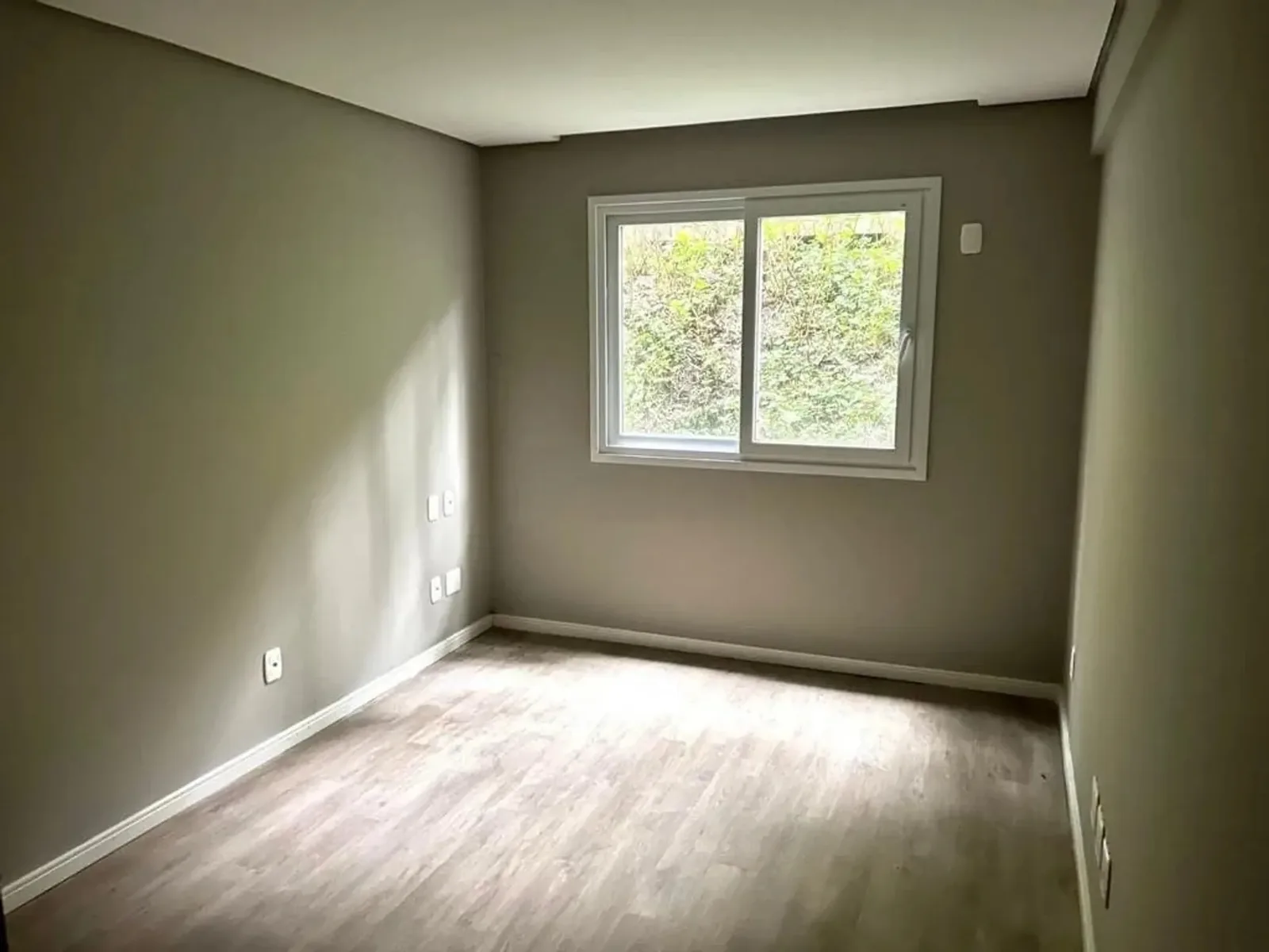 Dormitório vazio com janela para a mata e piso laminado