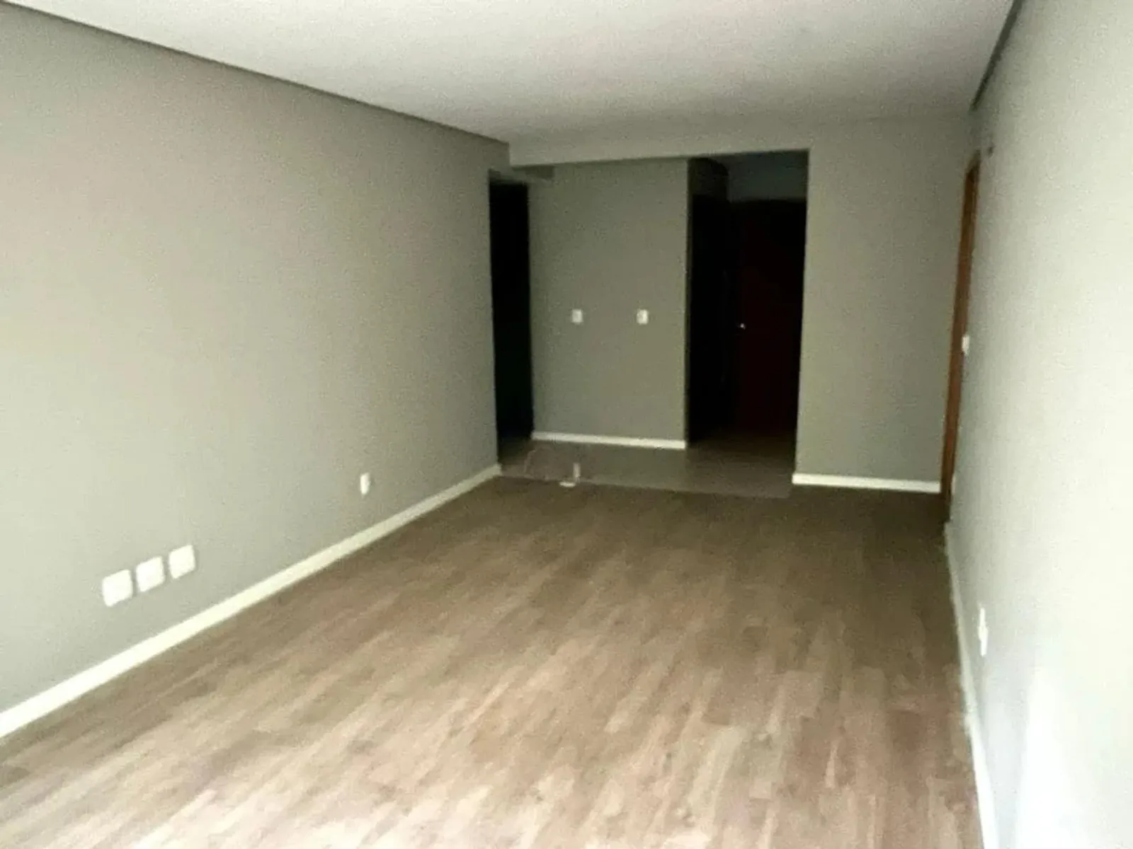 Sala e corredor vazios, com piso laminado e paredes em tom neutro