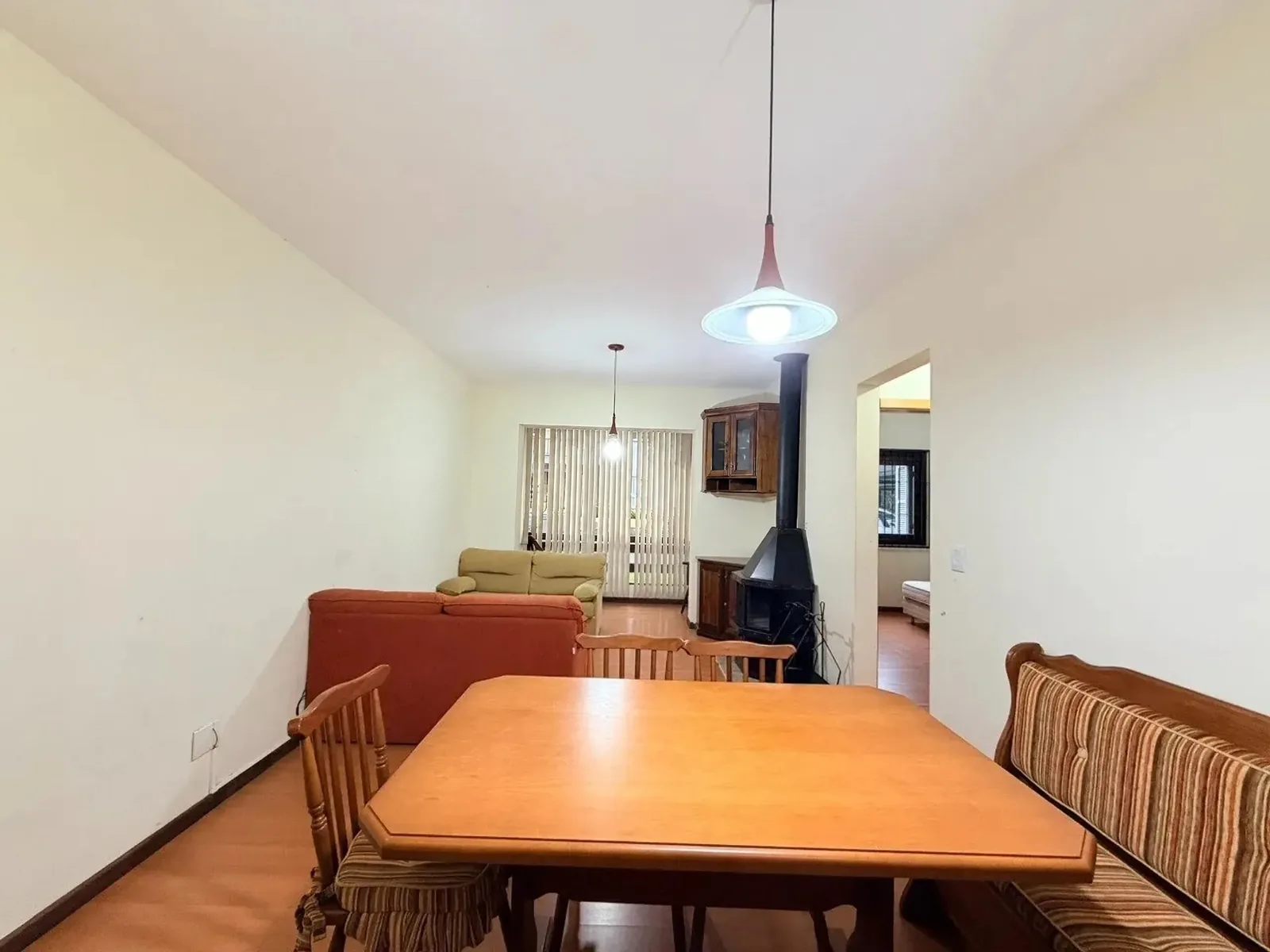 Sala de estar com sofás, lareira, cristaleira de canto e persianas na porta da sacada