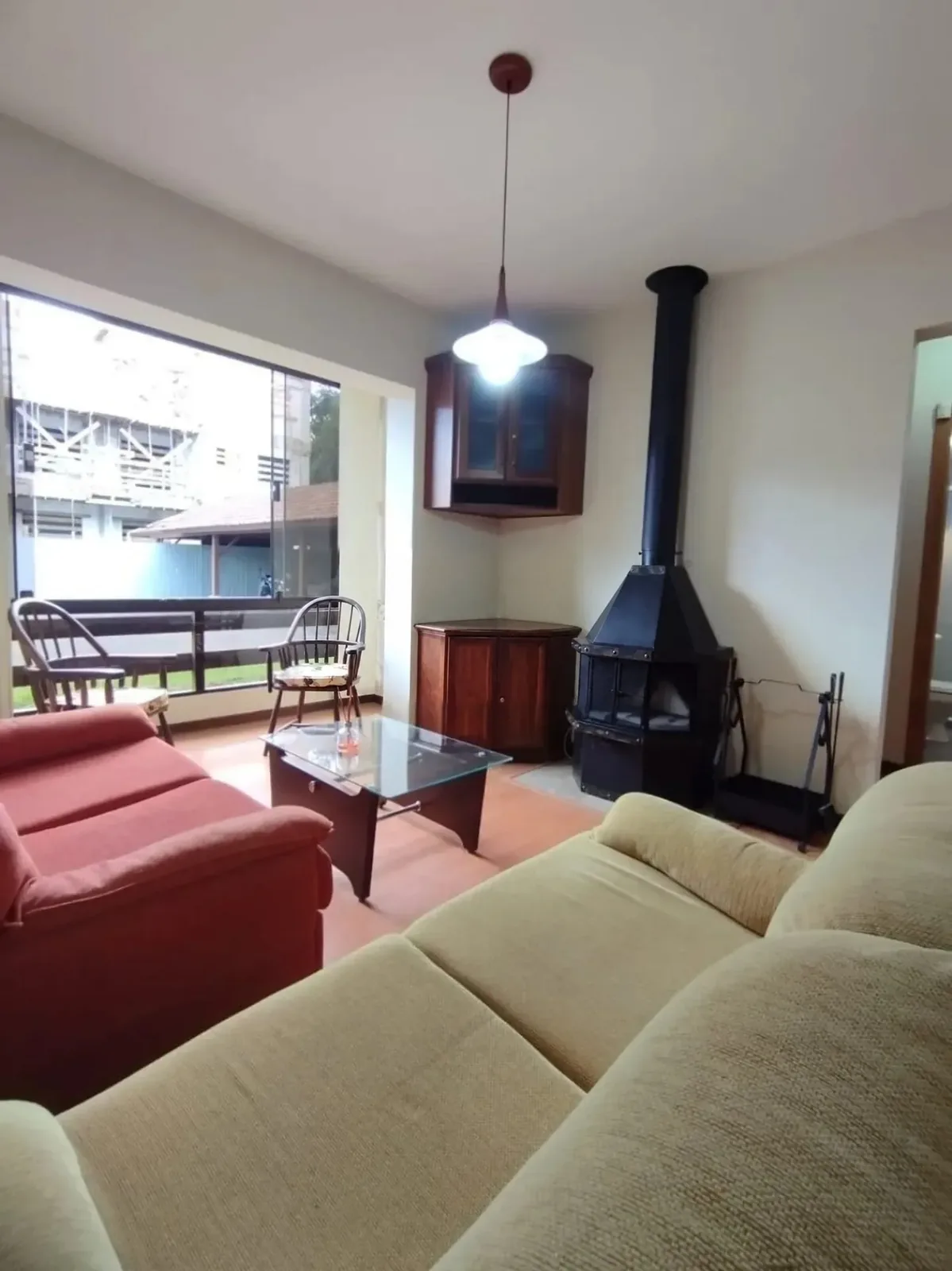 Sala com mesa de centro de vidro, cadeira de madeira, cristaleira e lareira junto à sacada