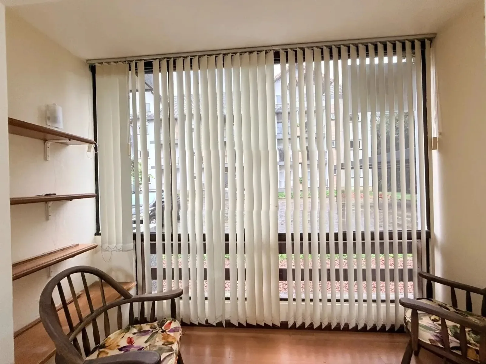 Porta da sacada com persianas verticais e vista para o jardim do condomínio