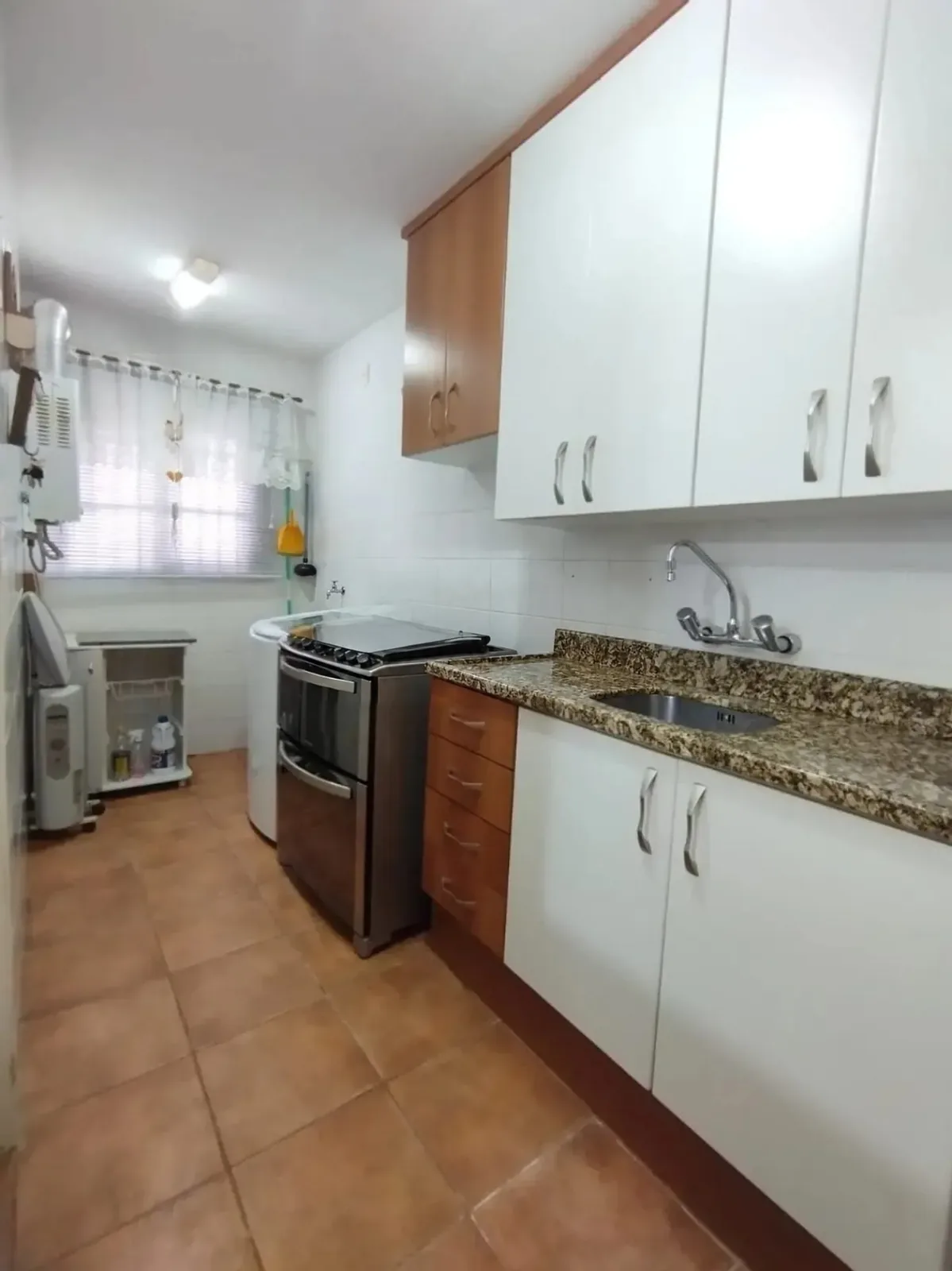 Cozinha com fogão de inox, bancada de granito e armários brancos e de madeira