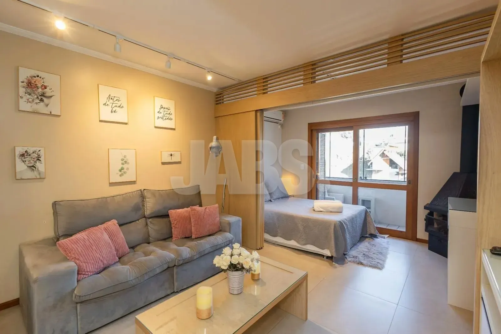 Sala com sofá, quadros na parede e portas de correr que abrem para o ambiente da cama