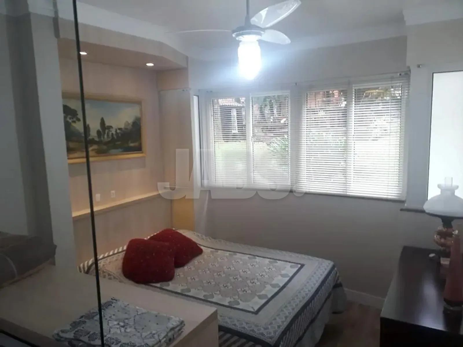 Cama de casal com almofadas vermelhas sob as janelas com persianas