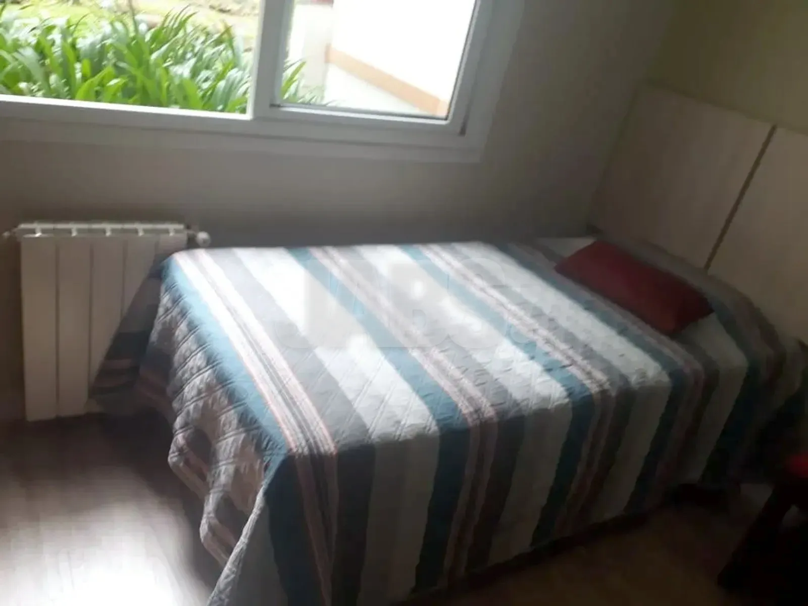 Dormitório com cama de casal, colcha listrada e janela para o verde
