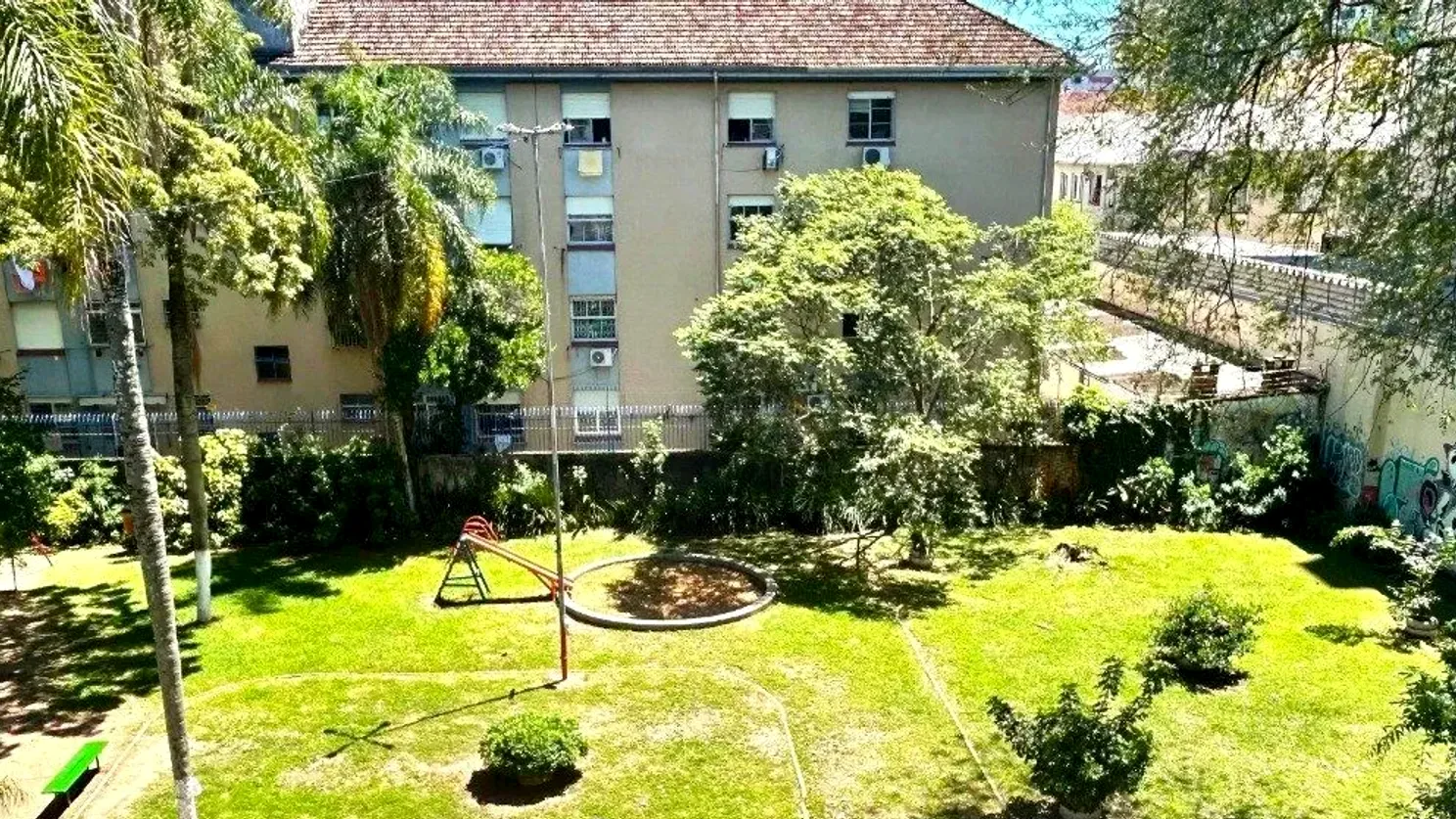 Pátio gramado e arborizado do condomínio, com área de brinquedos