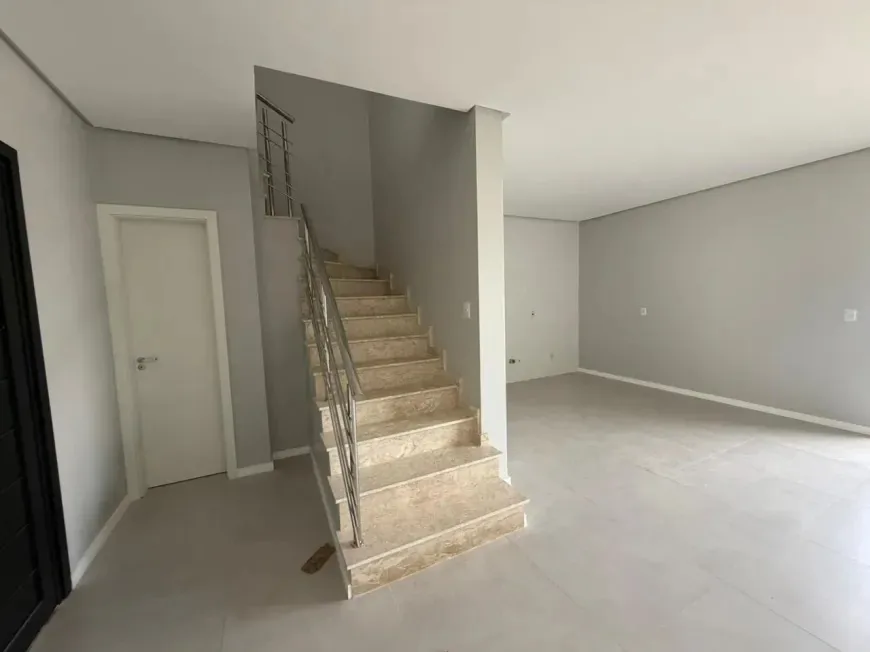 Escada interna com degraus em porcelanato e corrimão de inox, ao lado de porta branca