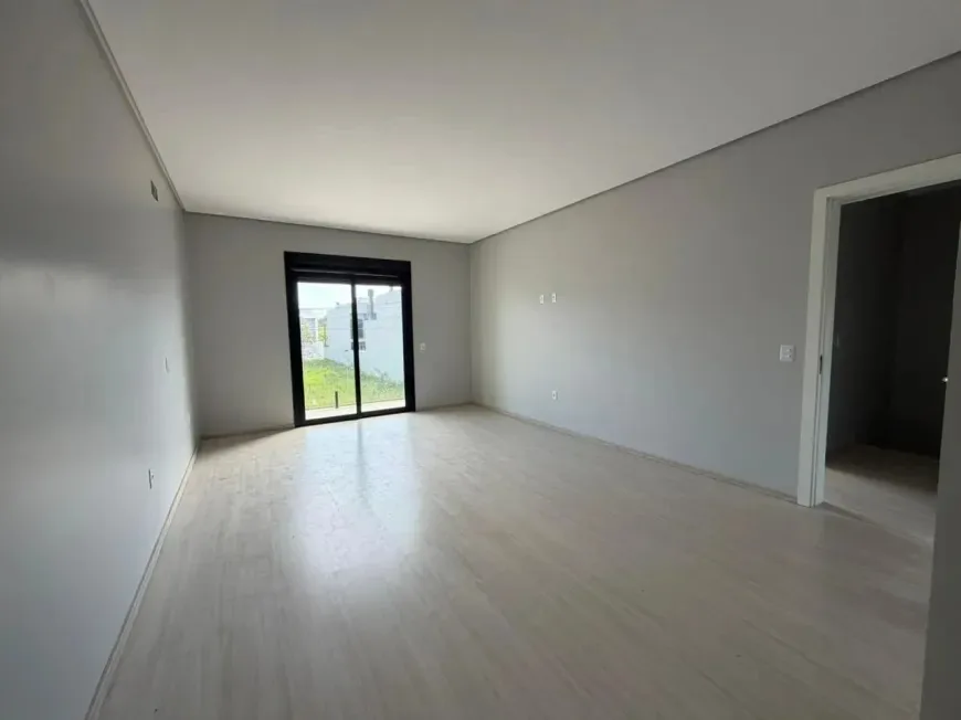 Dormitório vazio com piso laminado claro e porta de vidro de correr para a varanda